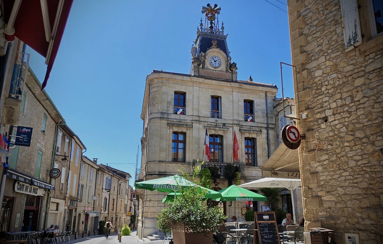 La mairie de Quissac et son horloge, vues depuis la rue, terrasses de café au premier plan